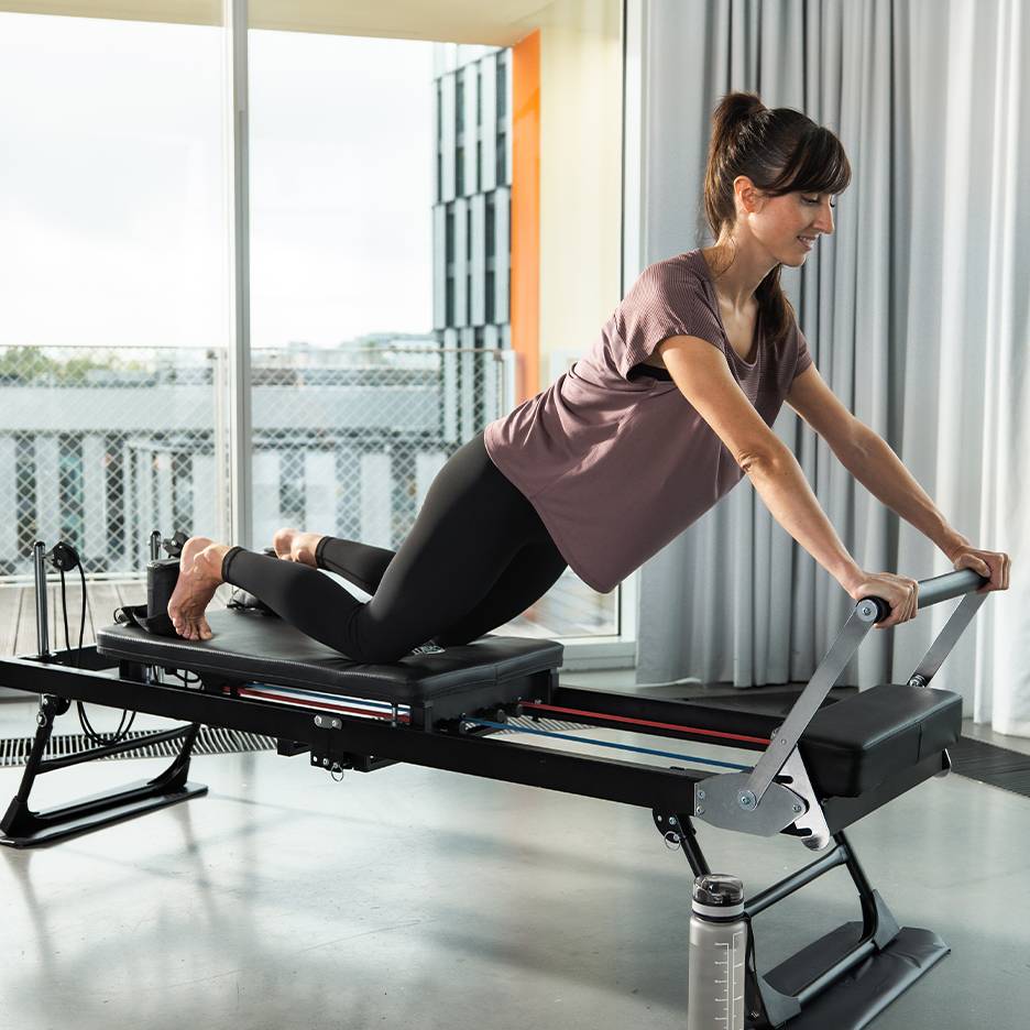 Kobieta ćwicząca Pilates na reformerze ze sprężynami i paskami.