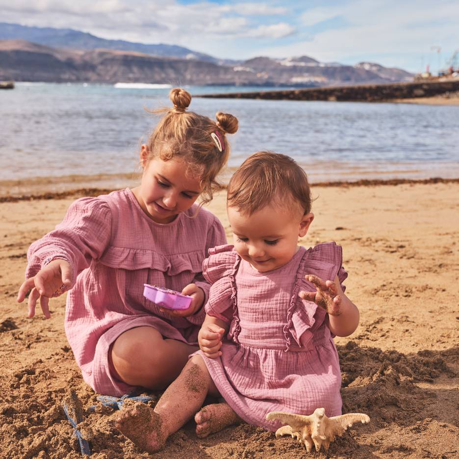 Dwie dziewczynki w różowych sukienkach bawią się w piasku na plaży.