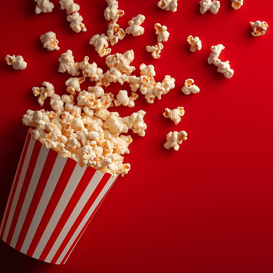 Popcorn na czerwonym tle, część popcornu w pasiastym kartonowym kubku.