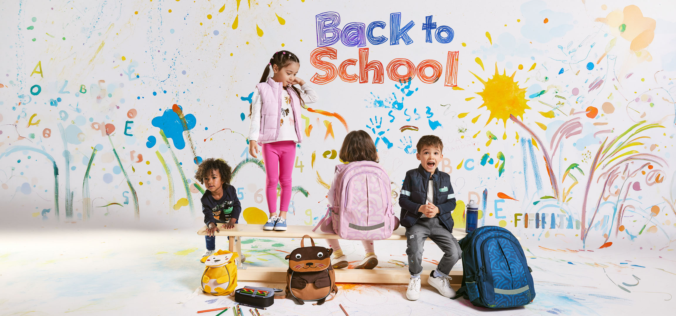 Dzieci z plecakami na tle kolorowego napisu „Back to School”.
