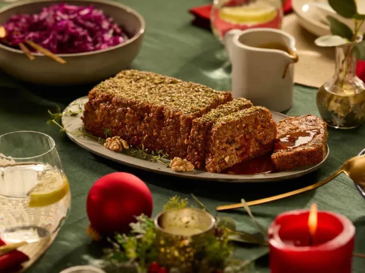 Pieczeń orzechowa z sosem, czerwoną kapustą i świątecznymi dekoracjami na zielonym obrusie.