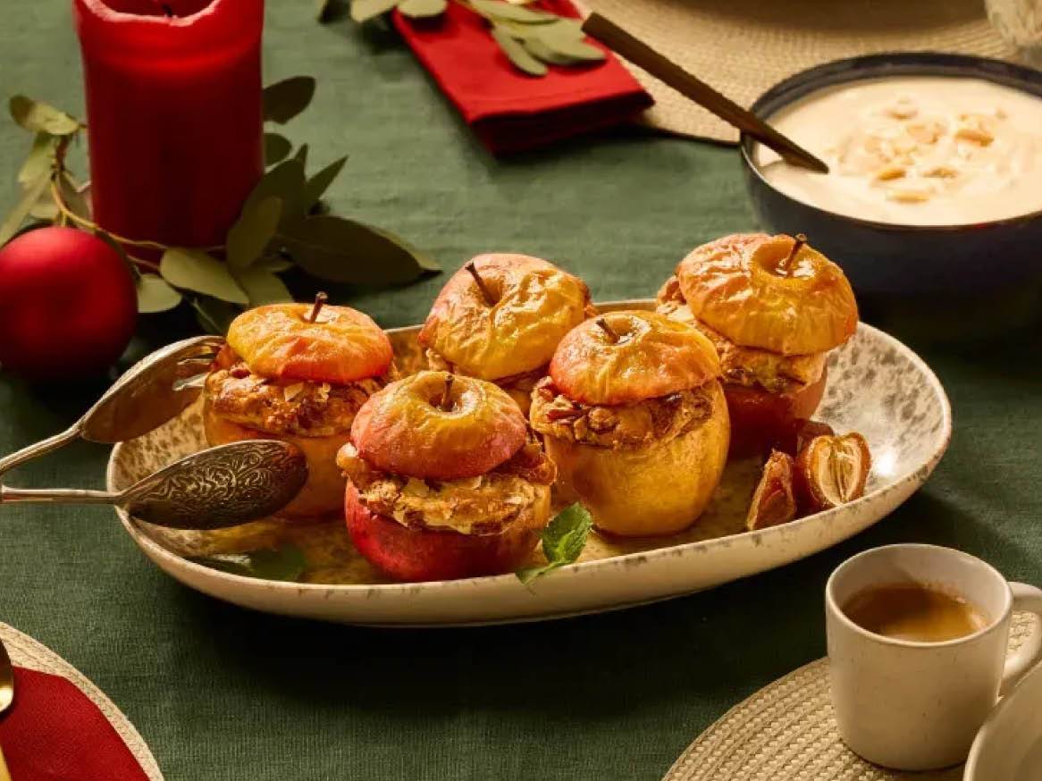 Pieczone jabłka z nadzieniem na świątecznym stole z czerwoną świecą i sosem.