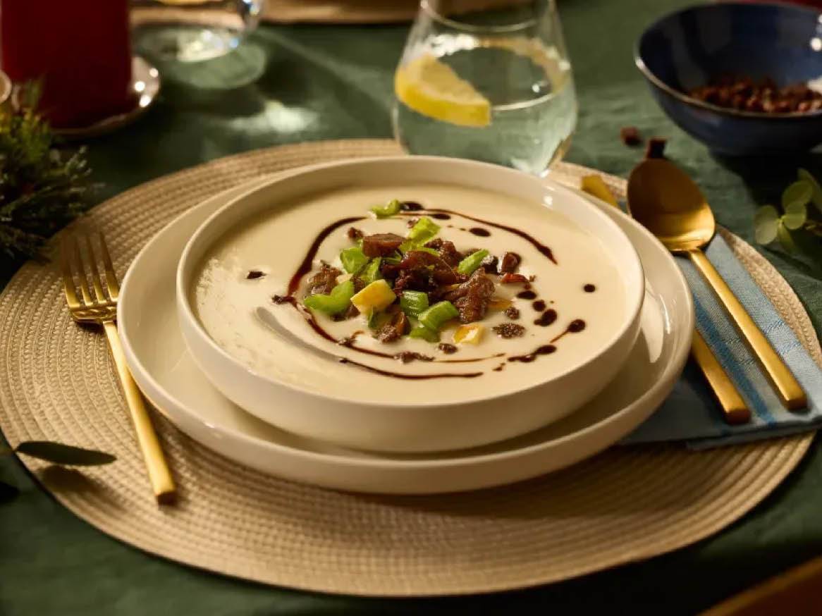 Kremowa zupa z kawałkami warzyw i sosem balsamicznym, podana na stole z nakryciem.