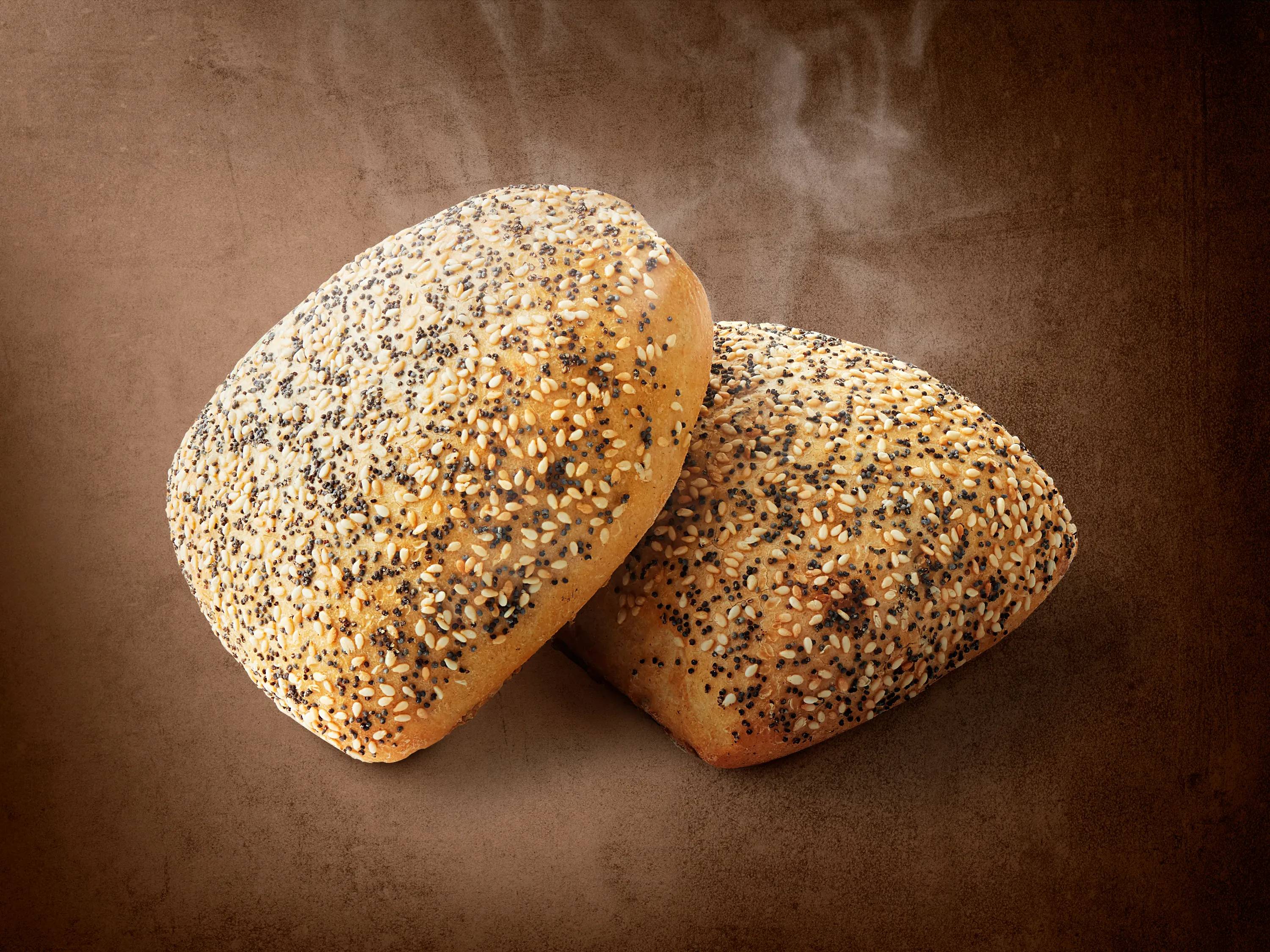 Dwie świeżo upieczone bułki z sezamem i makiem na brązowym tle.
